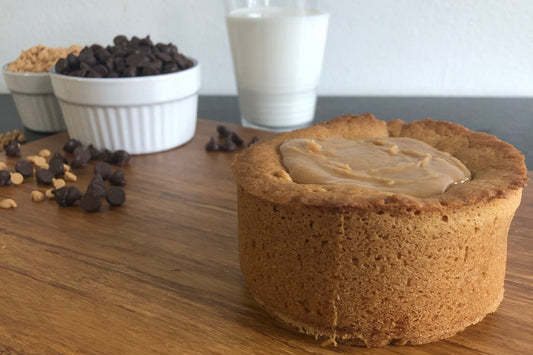 The PB Cup Beast from The Bearded Baker. Decadent peanut butter cup filling paired with Nutella, chocolate chips and peanut butter chips in a soft cookie dough pictured with a cold glass of milk and peanut butter and chocolate chips