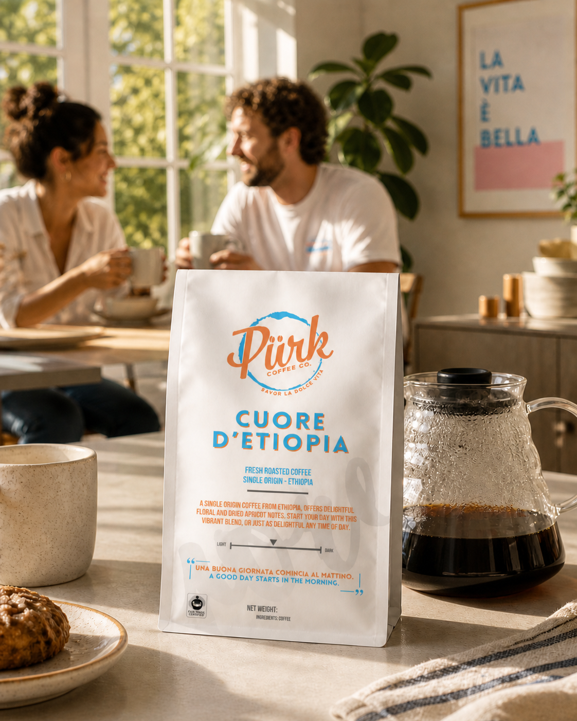 A bag of PÜRK Coffee Co's Cuore d'Etiopia sits on a table beside a fresh brewed pot of coffee while a couple sits in the background enjoying their morning brew